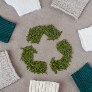 A collection of grey, white, and blue sweater sleeves, all in a circle around a recycling symbol made of grass.