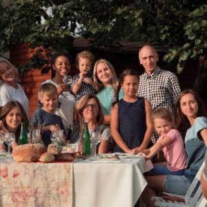 A group of people representing multiple generations sitting and standing around a table, smiling for a photo.