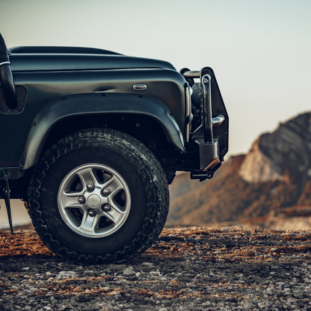 The front of an off-road vehicle sitting on rocky ground. There is a mountain in the background.
