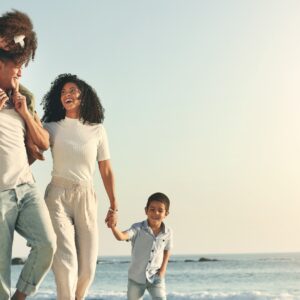 A joyful family of four, two parents and two small children, walking along a shoreline at a beach.