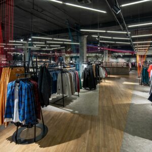 A wide view of the interior of a clothing retail store. The store is dimly lit with numerous racks with clothes on hangers.