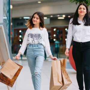 A teenage girl and her mother are smiling and laughing as they shop at the mall, holding many shopping bags.