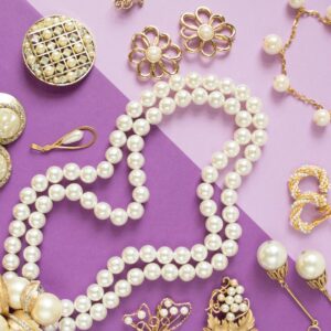 An assortment of pearl jewelry, including necklaces, bracelets, earrings, and brooches, on a purple surface.