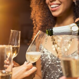 A close-up of someone pouring champagne out of the green bottle into a young woman's champagne flute.