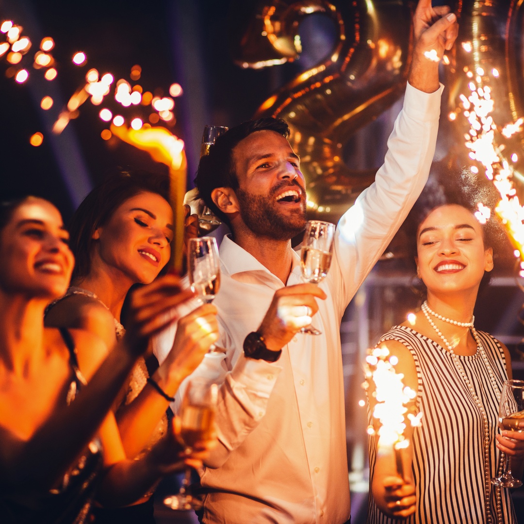 A group of friends cheering and enjoying the moment as they hold champagne and sparklers for the New Year.