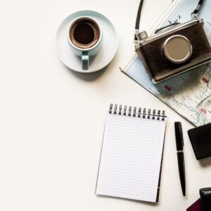A close-up of a travel map flat lay with map, camera, compass, coffee cup, wallet, passport and open notebook.