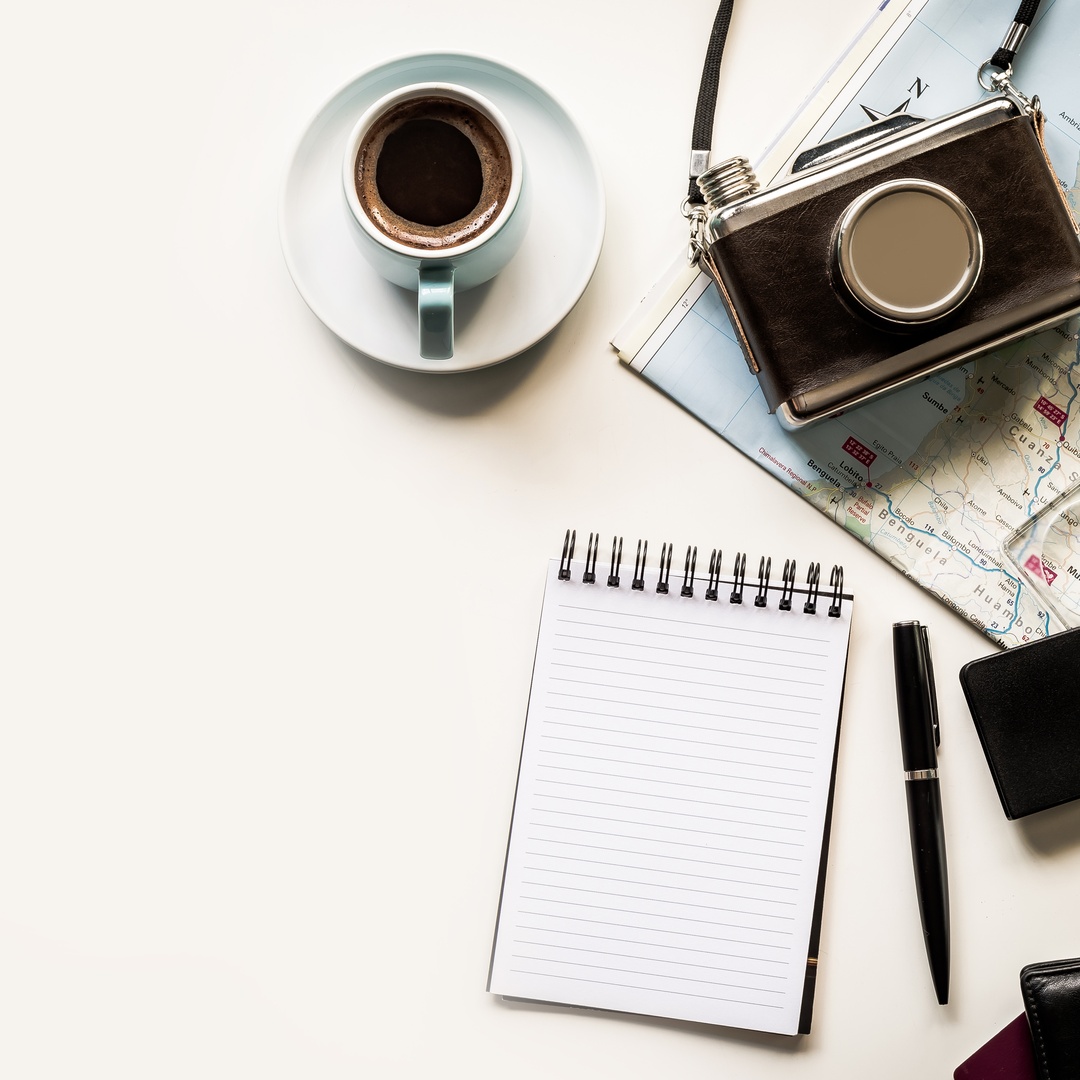 A close-up of a travel map flat lay with map, camera, compass, coffee cup, wallet, passport and open notebook.