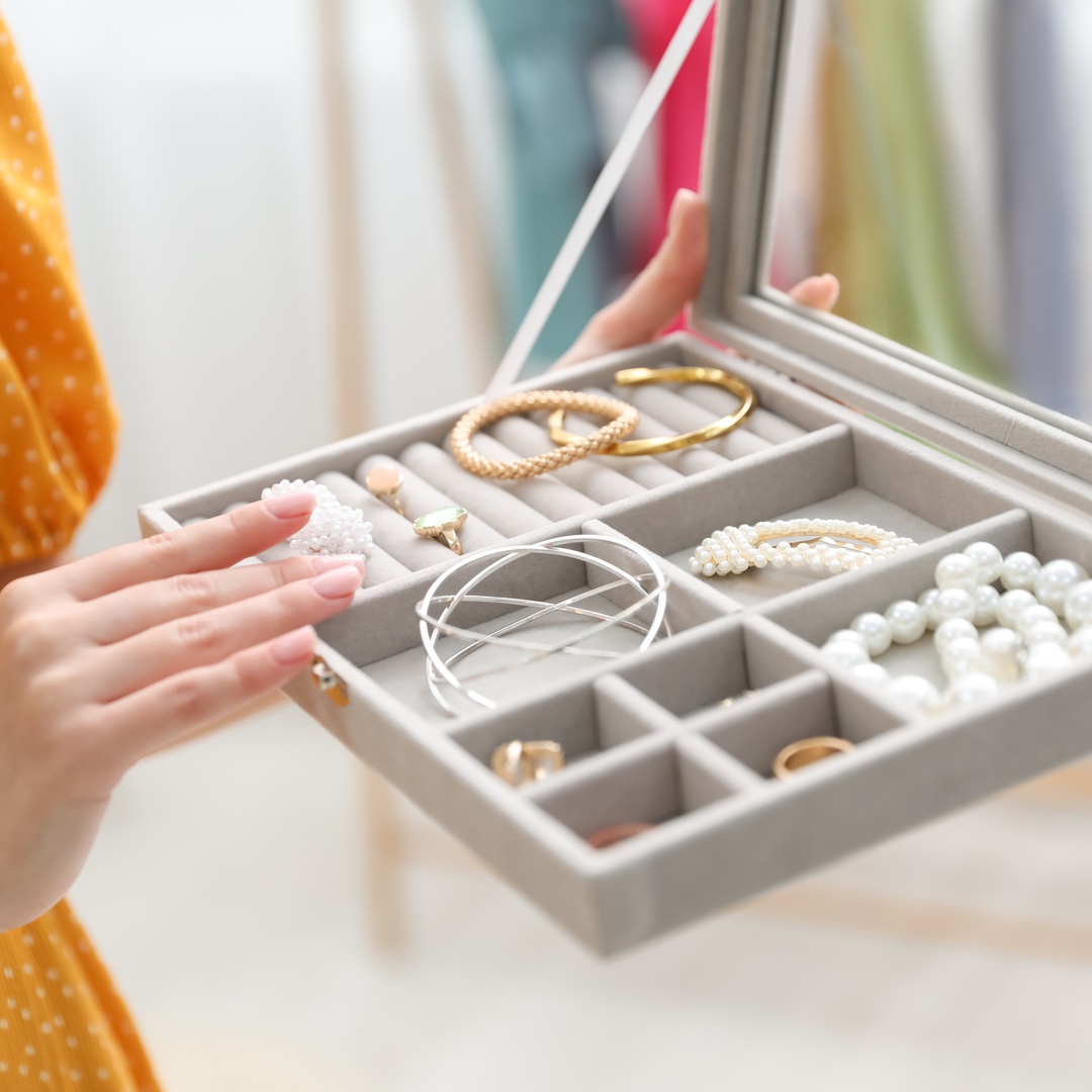 A person wearing a yellow polka-dot dress holds a jewelry box open with several gold, silver, and pearl pieces inside.