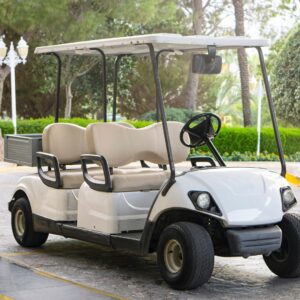 A large, white golf cart with four seats parked on a stone driveway. There are marble pillars on either side of it.