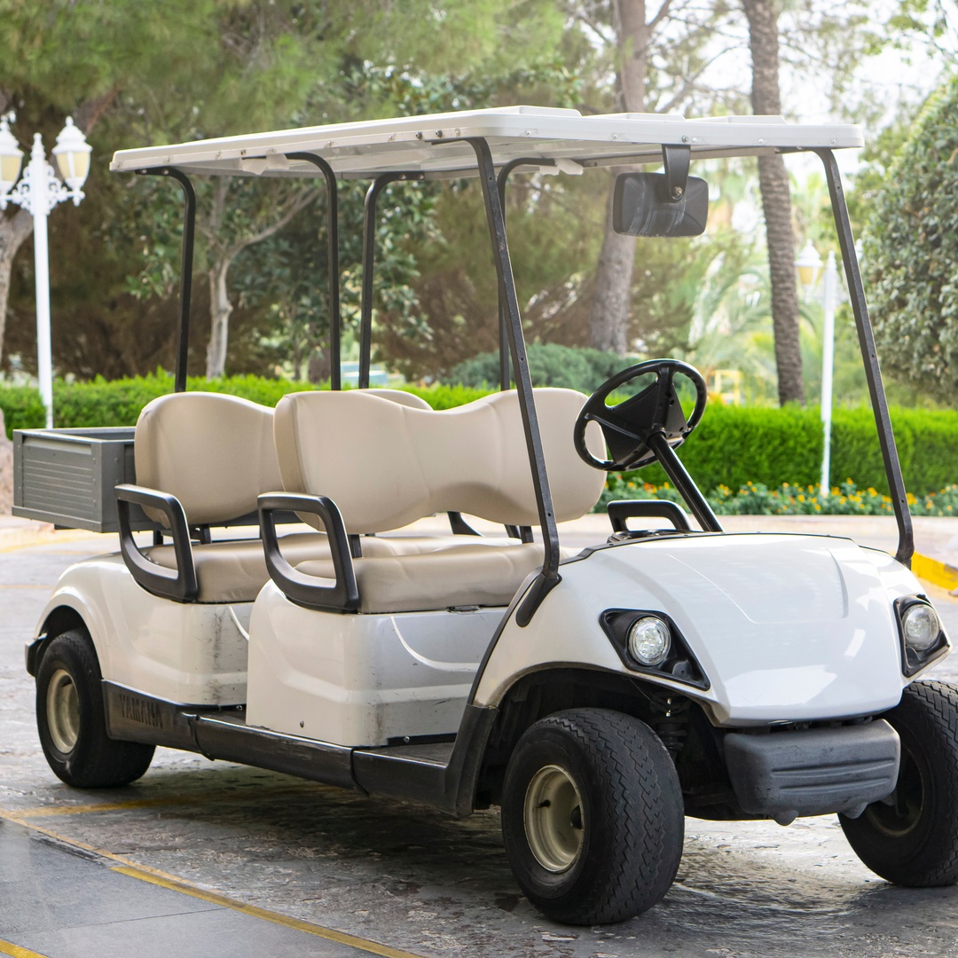 A large, white golf cart with four seats parked on a stone driveway. There are marble pillars on either side of it.