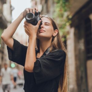A woman holding a digital camera up to her face. She is pointing the camera at the tall buildings that surround her.