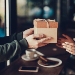 A close-up of someone handing someone else a small two-tone box with a carefully placed bow on top.