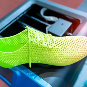 A close-up of a neon green 3D-printed tennis shoe resting on top of a black and blue 3D printer.