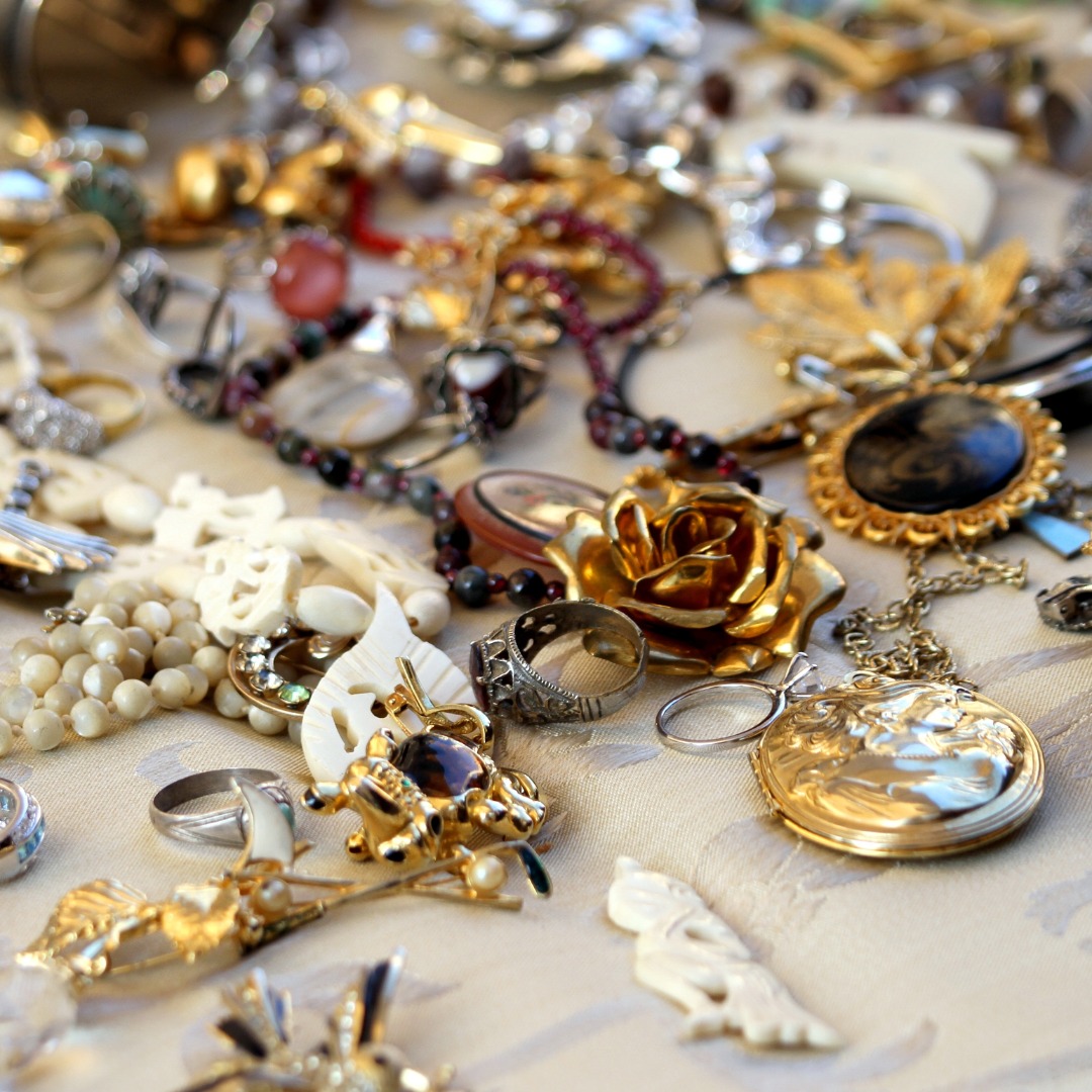Vintage jewelry including pearl necklaces, rings, brooches, and gold lockets displayed across a table at an antique market.