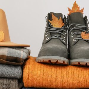 A pair of black fashion boots sits on top of an orange sweater. Other sweaters are next to the orange one.